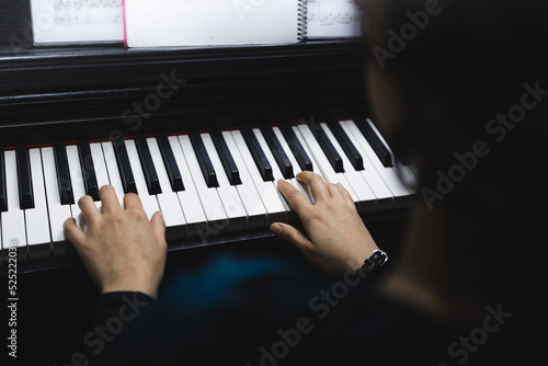 Rear view of woman's hands playing piano by reading sheet music. Selective focus