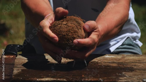 Close up of man holding coconut, cutting it in half with machete. Slow motion.