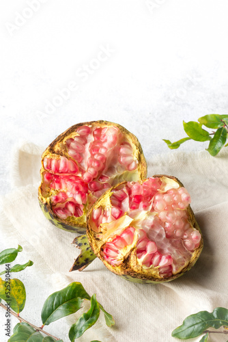 freshly harvested pomegranate on white surface with its leaves, sweet juicy fruit with edible seeds, taken in soft-focus background with copy space