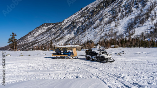Fotografi In a snowy valley there is a snowmobile with a sled attached