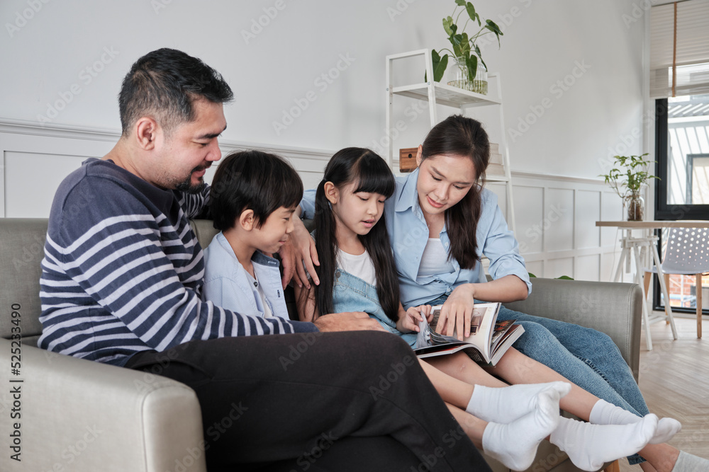 Asian Thai family, adult dad, mum, and children happiness home living relaxing activities and reading book together, leisure on sofa in white room house, lovely weekend, wellbeing domestic lifestyle. Asian Thai family, adult dad, mum, and children happiness home living relaxing activities and reading book together, leisure on sofa in white room house, lovely weekend, wellbeing domestic lifestyle.