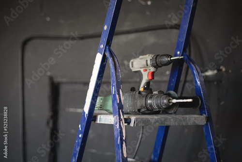 Perforator drill and handheld screwdriver on the stepladder background.