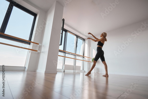 Fototapeta Naklejka Na Ścianę i Meble -  A beautiful girl is engaged in choreography. Doing a warm-up in a black tight-fitting suit. Dancing at the ballet barre
