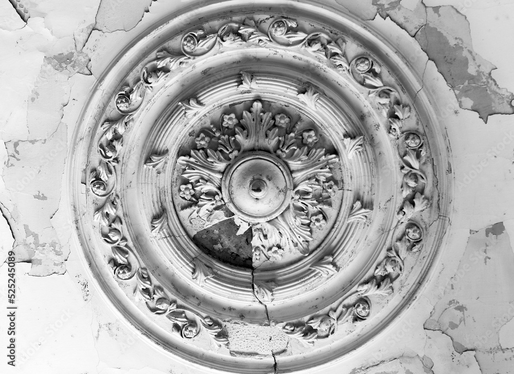 The old ceiling with crumbling plaster is decorated with stucco elements in the Baroque style - rosettes, volutes, floral ornaments. The old ceiling with crumbling plaster is decorated with stucco elements in the Baroque style - rosettes, volutes, floral ornaments.