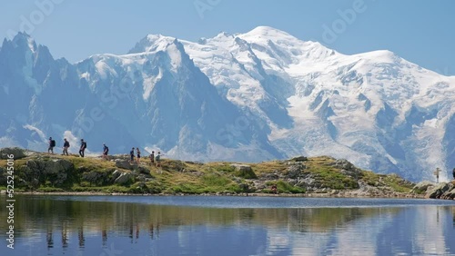 people hiking with reflections of the mountains, and behind the view of the mont blanc, in the valley of chamonix, in france in a sunny day. Static shoot.