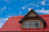 Red roof with dormer in the blue sky background. Decorative metal roof. Types of roof roofs. Roofing