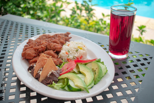 pechuga de pollo empanizada con arroz ensalada y frijoles acompañado de agua de jamaica en un fondo vacacional photo