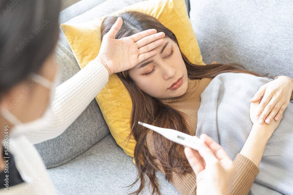 Naklejka premium Sick, influenza asian young woman, girl headache have high fever, flu check thermometer measure body temperature, feel illness while sitting on sofa, couch at home. Health care, infection of covid-19.