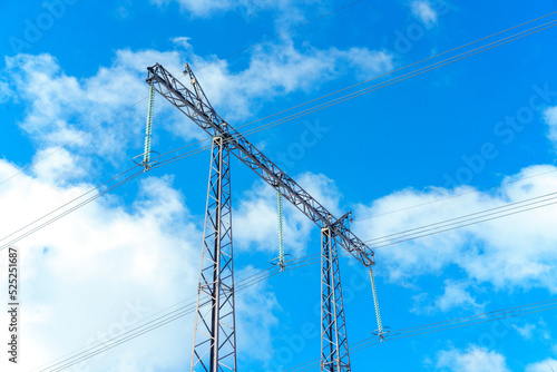 High voltage lines and power pylons on a sunny day with clouds in the blue sky. 
