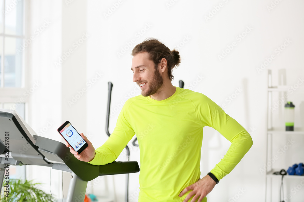 Sporty young man using phone with installed app for calories counting in gym