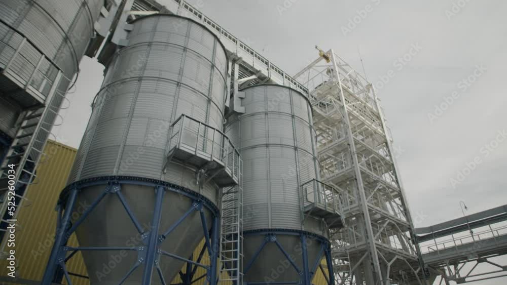 A line of steel grain silos for storing cereal crops harvest, hopper bins, wheat storage. industrial scene, low angle view, ooutdoors A line of steel grain silos for storing cereal crops harvest, hopper bins, wheat storage. industrial scene, low angle view, ooutdoors