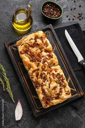 Wooden board with tasty Italian focaccia, jug of oil and peppercorns on dark background