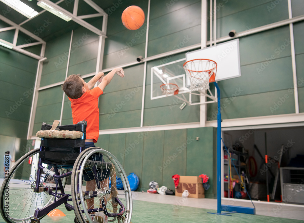 Boy in a wheelchair throwing the ball into the basketball basket Stock