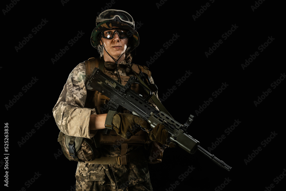 Woman army soldier in combat uniforms with assault rifle, plate carrier, goggles and backpack. Studio shot, dark background Woman army soldier in combat uniforms with assault rifle, plate carrier, goggles and backpack. Studio shot, dark background