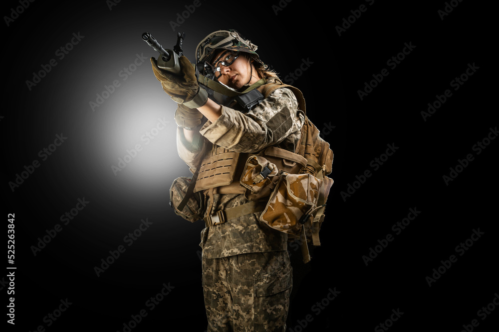 Woman army soldier in combat uniforms with assault rifle, plate carrier, goggles and backpack. Studio shot, dark background