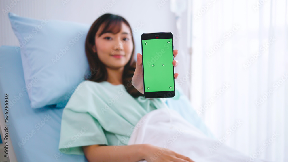 Happy young Asian female patient showing smartphone with green screen during hospitalization. Happy young Asian female patient showing smartphone with green screen during hospitalization.
