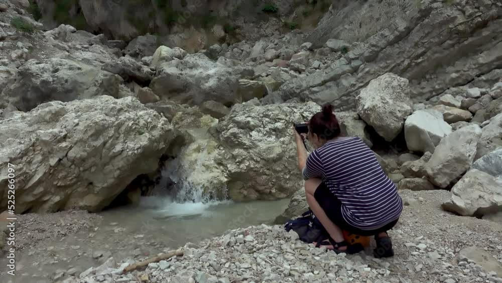 Hiker woman photographer in a rocky valley with spring stream water in the mountain river. Photographer hiker taking pictures of nature. Hiker woman photographer in a rocky valley with spring stream water in the mountain river. Photographer hiker taking pictures of nature.