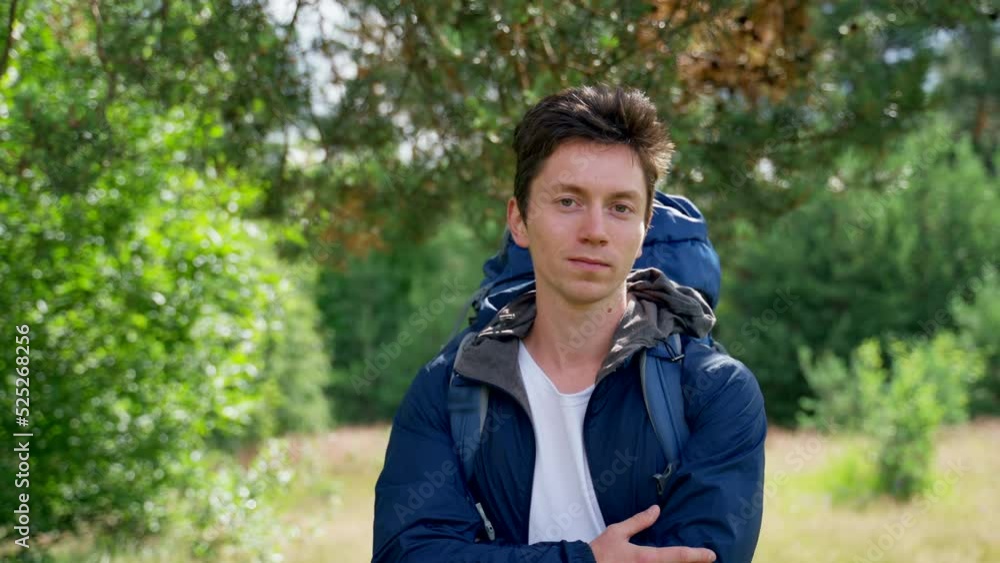 Young man hiker stands on green forest glade looking around for footpath for hiking. Black-haired tourist enjoys walking uniting with forest nature Young man hiker stands on green forest glade looking around for footpath for hiking. Black-haired tourist enjoys walking uniting with forest nature