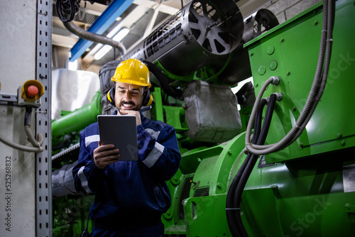 Experienced serviceman engineer with digital tablet checking gas generator in power plant.