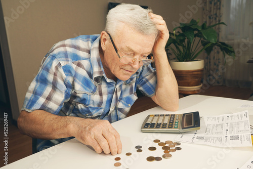  Upset depressed Senior man sitting at the table and calculating finances. Old man checking bills. Man counting coins on the table. Pension calculation concept