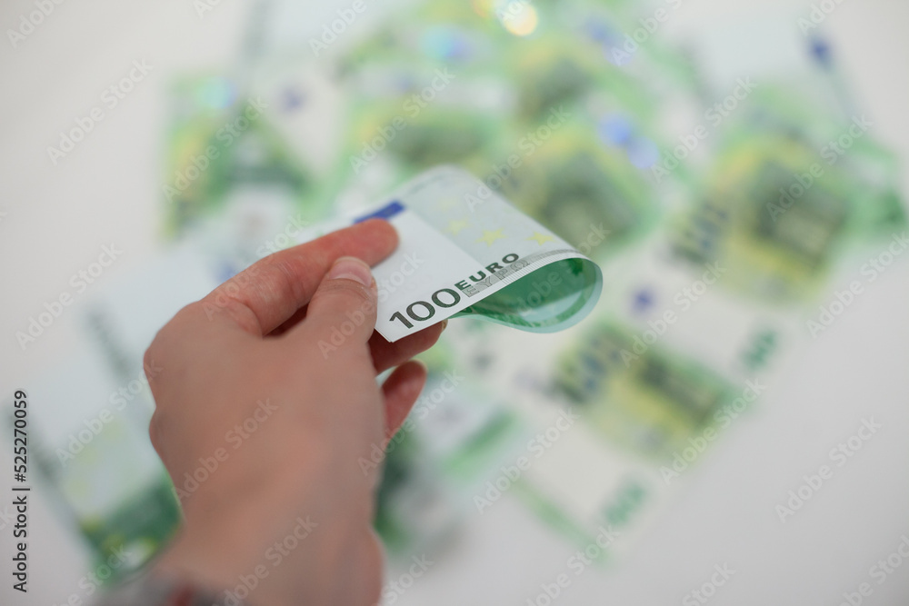 Hand holding 100 euro money banknotes on blurred money background. Multiple one hundred euro notes in pile or group. Investment and inflation in Europe concept.