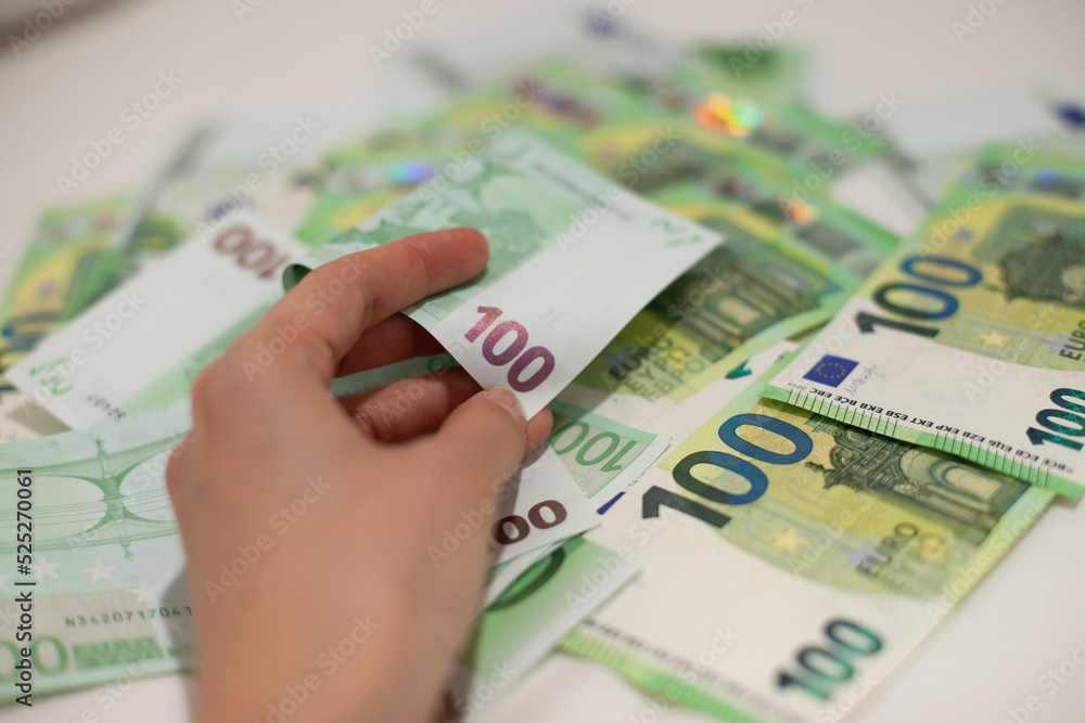 Hand holding 100 euro money banknotes on blurred money background. Multiple one hundred euro notes in pile or group. Investment and inflation in Europe concept.