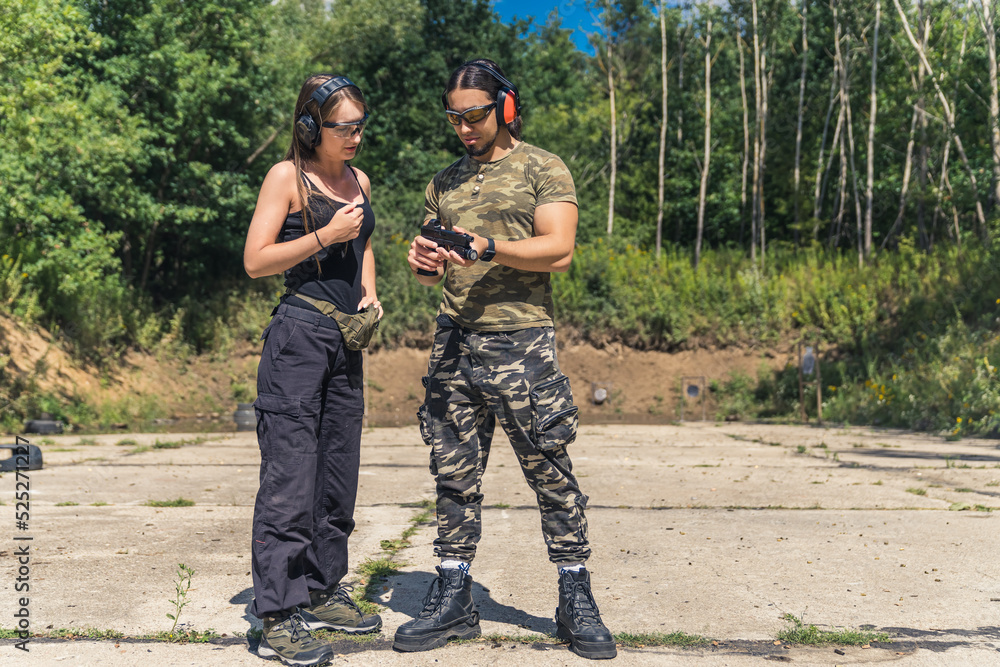 Private shooting lesson at a nearby outdoor gun range. Two people in moro military-like clothes. Caucasian male instructor and caucasian woman. Full length shot. High quality photo