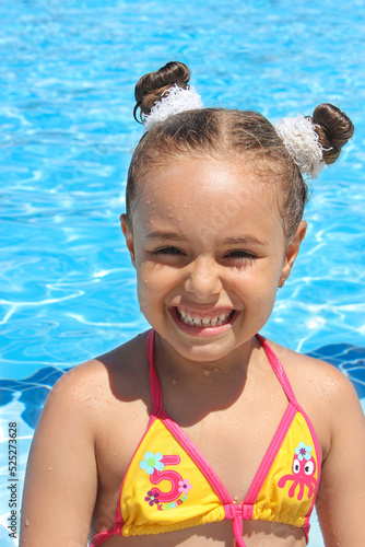 Happy little girl in the pool. Smiling baby girl in a swimming suit and with a funny hairstyle