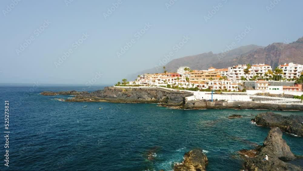 Aerial view of deserted rocks and black volcanic beach. Cityscape with hotels, white resort houses, buildings. Blue sky. Deep ocean. Tenerife, Canaries, Spain. Spectacular nature landscape. Aerial view of deserted rocks and black volcanic beach. Cityscape with hotels, white resort houses, buildings. Blue sky. Deep ocean. Tenerife, Canaries, Spain. Spectacular nature landscape.