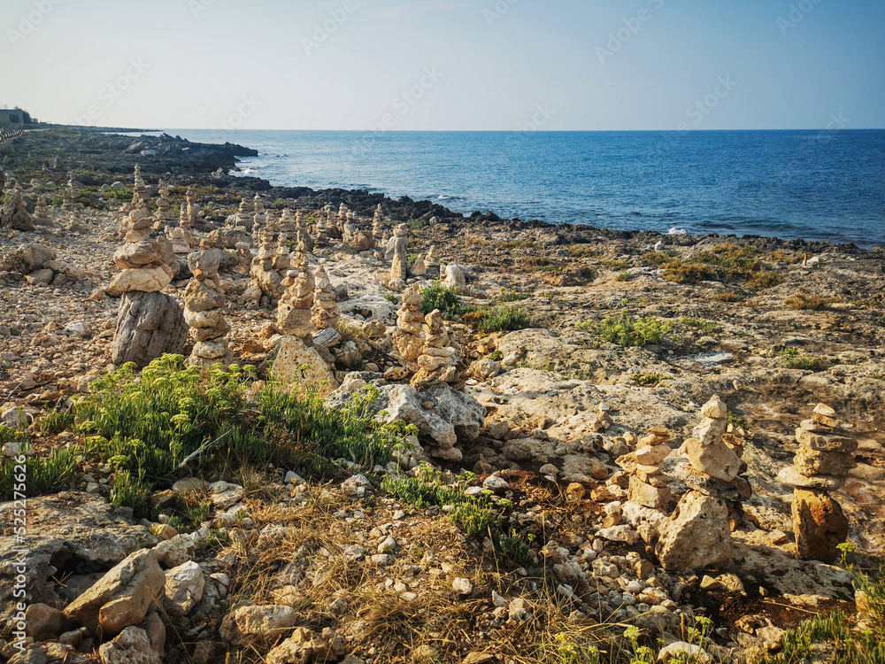 Rocky shore of Capilungo, Salento, Puglia, Southern Italy, with cairns and vegetation, in a sunny summer day, with bright colors, clear water and blue sky. 