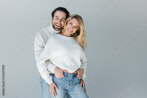 happy couple in white sweaters and denim jeans posing isolated on grey