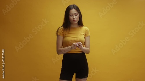 A young Asian woman putting lots of chewing gum into her mouth, in front of a yellow background photo