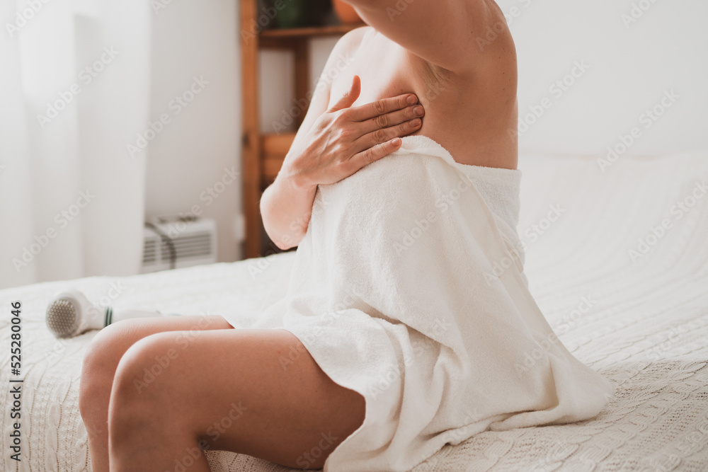 Obraz premium Young woman examines her breasts and lymph nodes with her hands while sitting at home in the bedroom