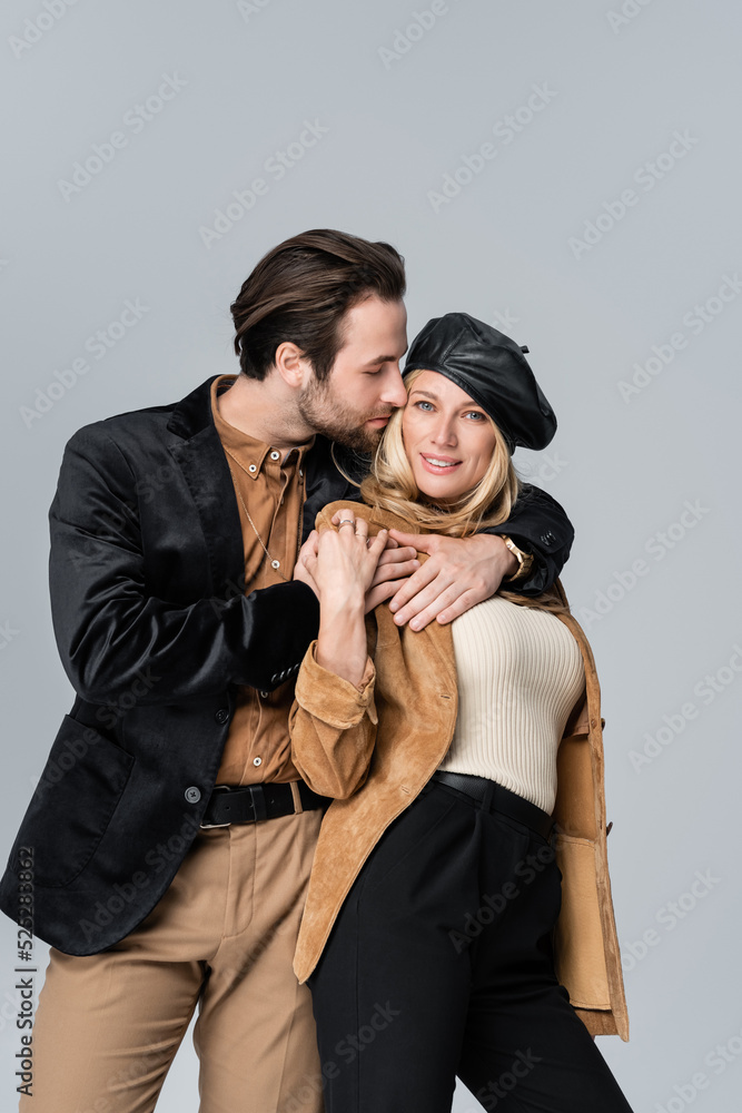 cheerful man hugging happy woman in stylish beret isolated on grey cheerful man hugging happy woman in stylish beret isolated on grey