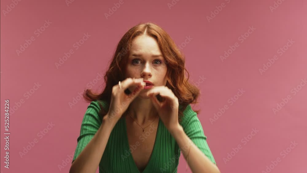 A young white ginger woman, using hand binoculars, rubbing eyes in disbelief and amazement, in front of a pink background wearing a green dress A young white ginger woman, using hand binoculars, rubbing eyes in disbelief and amazement, in front of a pink background wearing a green dress