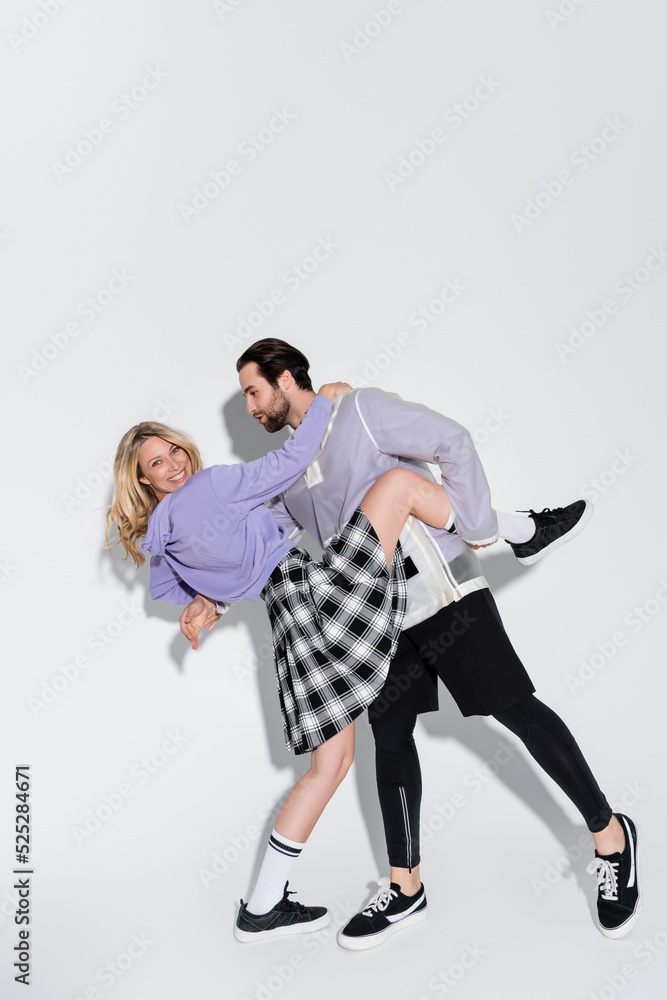 full length of bearded man holding leg of happy blonde woman in tartan skirt on grey full length of bearded man holding leg of happy blonde woman in tartan skirt on grey