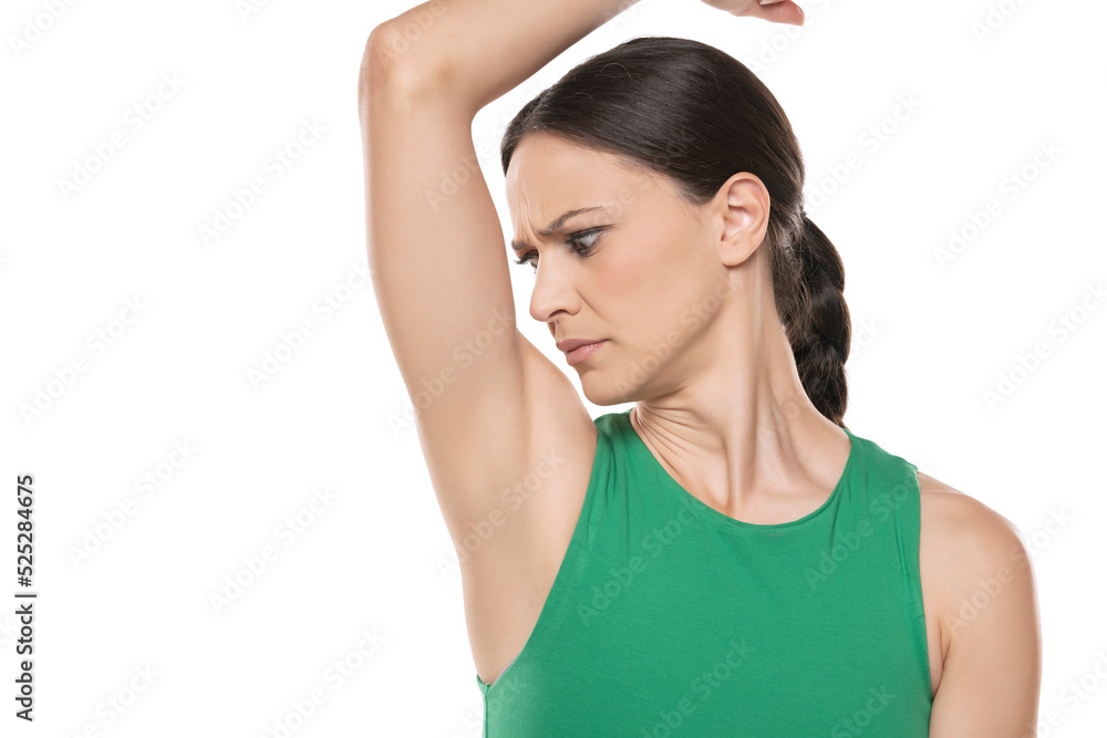 A young worried woman smells her underarm. on a white background A young worried woman smells her underarm. on a white background