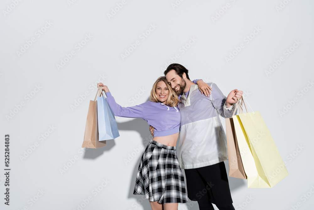 happy man and blonde woman in tartan skirt holding shopping bags on grey