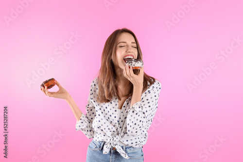 Beautiful young woman with donuts on light pink background photo