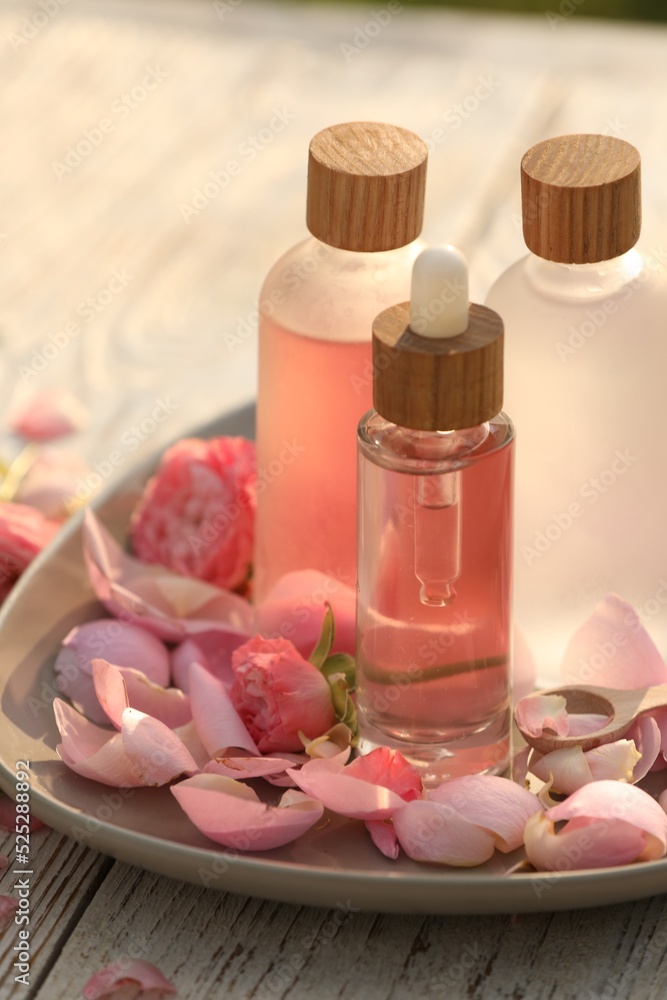 Bottles of rose essential oil and flowers on white wooden table, closeup Bottles of rose essential oil and flowers on white wooden table, closeup