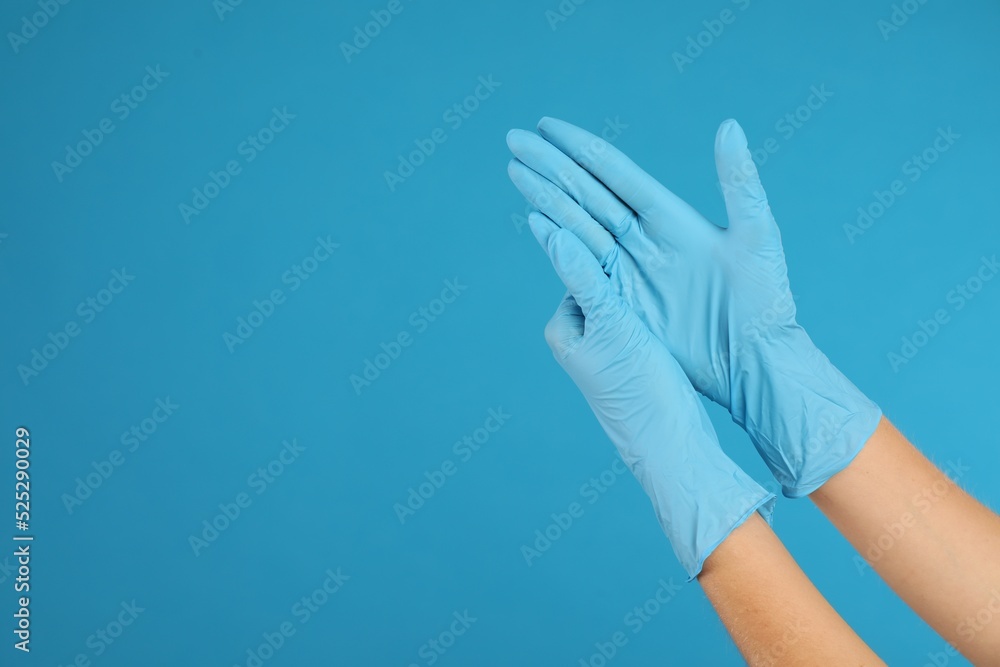 Doctor wearing medical gloves on light blue background, closeup. Space for text Doctor wearing medical gloves on light blue background, closeup. Space for text