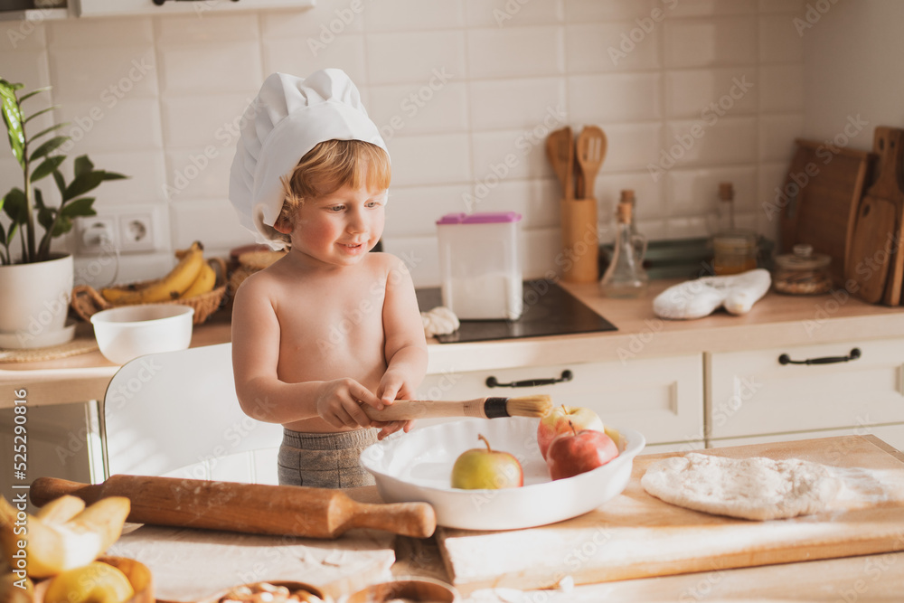 little boy of two years old in little chef's hat is preparing pie at home in kitchen little boy of two years old in little chef's hat is preparing pie at home in kitchen