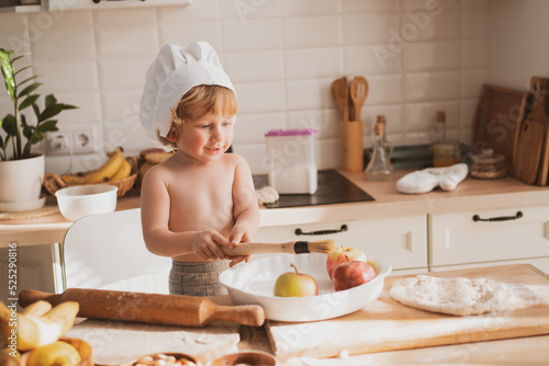 little boy of two years old in little chef's hat is preparing pie at home in kitchen