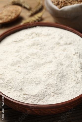 Wheat flour in bowl on wooden table, closeup