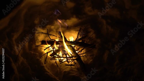 Person Adding Logs to a Fire in a Hole in the Snow during a Cold Winter Night in the Alps photo