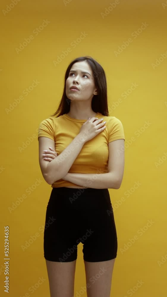 A young asian woman on a yellow background pointing up A young asian woman on a yellow background pointing up