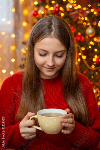 Portrait of smiling young blond girl in warm red sweater holding a cup of tea in her hands. Christmas and new year time, making herself warm and cozy feeling