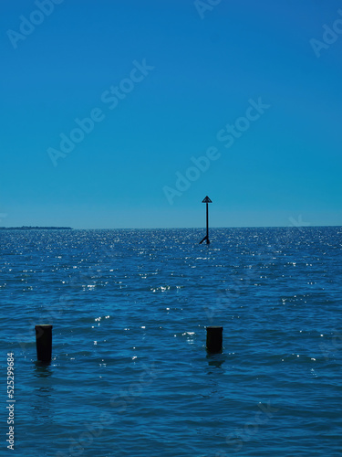 A minimalist seascape, with the silhouette of a market and a near-submerged groyne breaking up the varied blueness. © Das