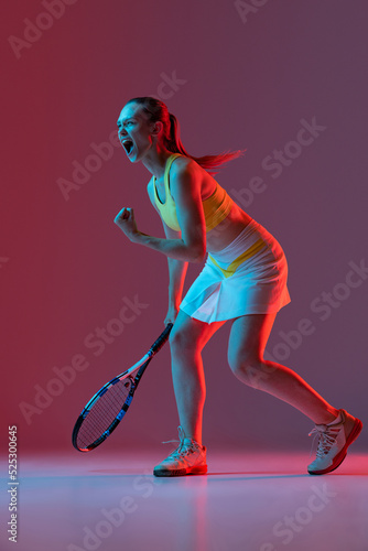 Excited young woman, tennis player shouting after sports win isolated on dark background in neon. Healthy lifestyle, fitness, sport, exercise concept. © master1305