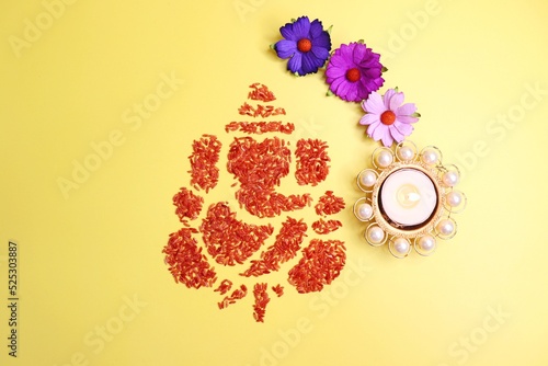 Ganesha art is made with colored rice. Ganesh Chaturthi wallpaper or banner. Ganpati face over yellow background along with diya and flowers. copy space. 